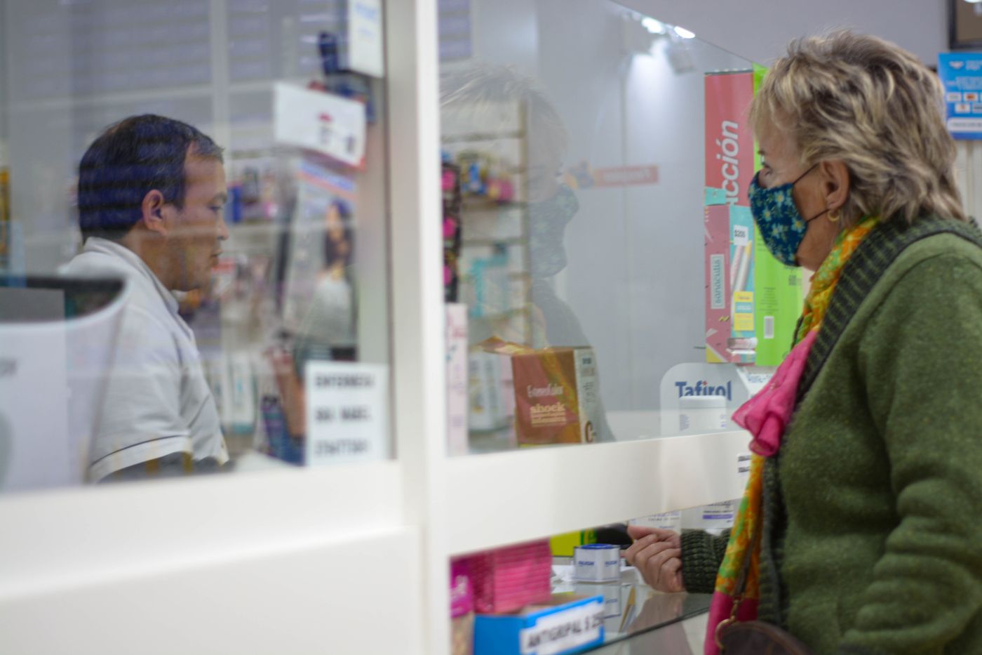 A customer wearing a face mask talks to a pharmacist across a pharmacy counter